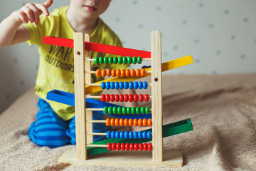 Preschooler baby learns to count. Cute child playing with abacus toy. Little boy having fun indoors at home, kindergarten or day care centre. Educational concept for preschool kids.