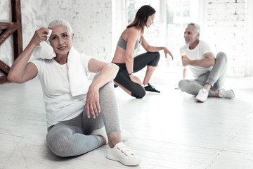 Obraz premium Active living. Positive minded senior lady smiling while wiping her forehead and enjoying a training session at a fitness club.