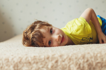 Beautiful little boy lying on bed and looking. Curly cute toddler