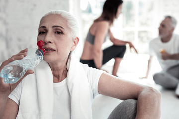 Don t forget about water. Pensive retired lady taking a break and drinking her water after taking part in an intense training session.