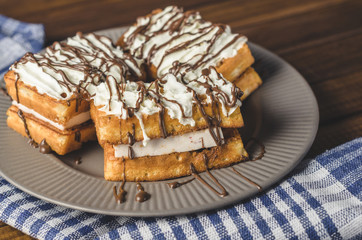 waffles with cream and chocolate on plate on wooden table.
