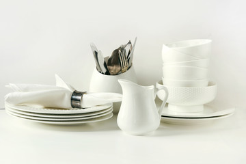 White tableware for serving. Crockery,dish, utensils and other different white stuff on white table-top. Kitchen still life as background. Copy space.
