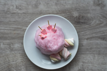 Composition of pink sweet cotton wool with hearts on wooden sticks and colorful souffle on a wooden background. Sweet entertainment for children and their parents. Culinary delights Valentine's Day