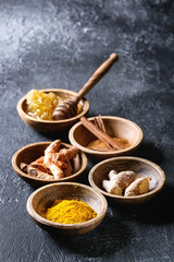 Ingredients for turmeric latte. Ground turmeric, curcuma root, cinnamon, ginger, honeycombs in wooden bowls over black texture background. Copy space