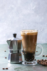 Fizzy iced Coffee espresso with milk, coffee maker and roasted beans around over grey green texture table. Modern drink. Copy space