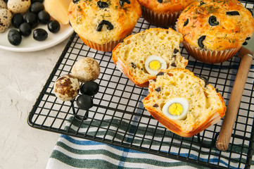 Savory muffins with olives, quail eggs and herbs on a wire rack on a white stone backdrop. Rustic style.