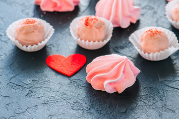 White chocolate strawberry truffles and pink meringue kisses on black stone background