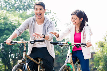 Obraz premium Young Asian couple laughing together while riding bicycles outdoors in summer 
