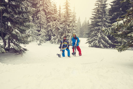 Joyful snowboarders relax amidst huge snow-covered fir trees