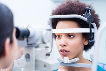 Optician measuring women eyes with refractometer in optician shop