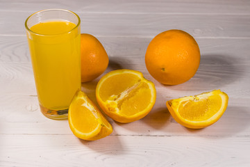 Glass of orange juice and fresh oranges on white wooden table