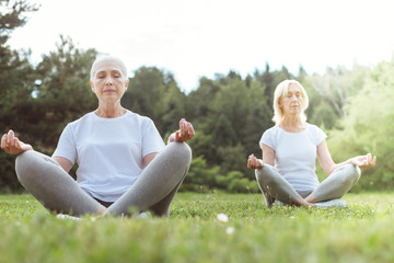 Inner peace. Nice calm elderly women sitting in the lotus pose and closing their eyes while practicing yoga