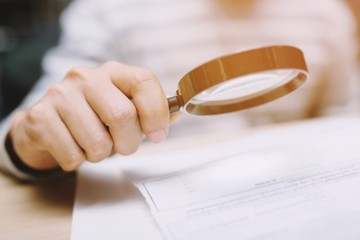 close up hand man looking through a magnifying glass to documents notebook notepad.