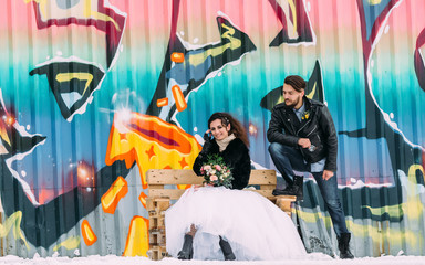 Wedding in the style of rock. Rocker or Biker wedding. Guys with stylish leather jackets. It's a rock'n'roll baby! A sweet couple is photographed against the background of graffiti.