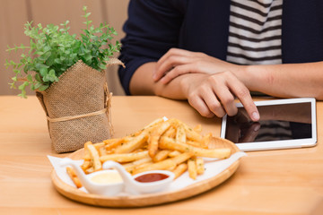 Hand of business woman working on electronic devices tablet with French fries on table