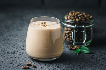 Espresso maca banana smoothie and coffee beans in glass jar on dark concrete background. Selective...