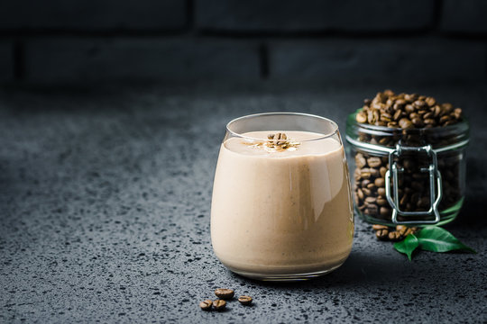 Vegan coconut milk banana coffee smoothie and coffee beans in glass jar on dark concrete background. Selective focus, space for text. 
