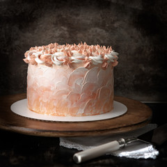 Tasty cake with orange frosting on a wooden stand and cake cutter. Brown background.Birthday...