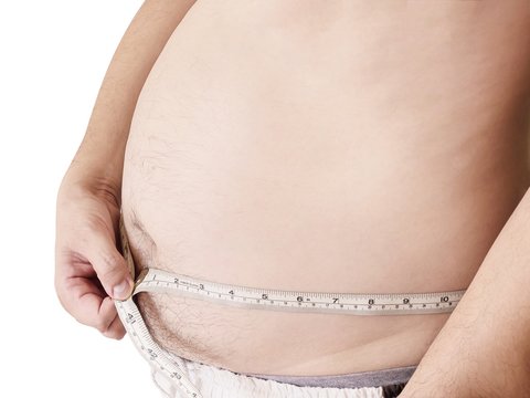 Fat man is measuring his belly using tape meter - dietary health concept