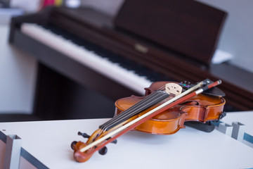 Fototapeta na wymiar Violin and bow on table with blured brown piano in background