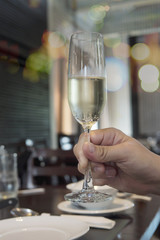 man hand holding champagne glass ready to drink over blur bokeh restaurant - people in party happy celebration concept