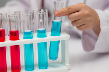 Hand of a chemist picking up blue liquid tube from tube's rack on the table..