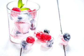 Frozen berries in glass for cocktail on wooden table background