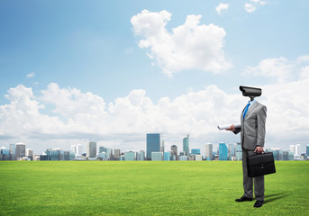 Camera headed man standing on green grass against modern cityscape