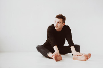 A young man, a student sits on the floor, against a white wall background, a pensive look. The guy is a model.