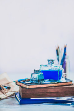 Retro creative writing concept with inkwells on a stack of drafts, pencil boxes and papers. High key still life. Writer workplace with a light background.