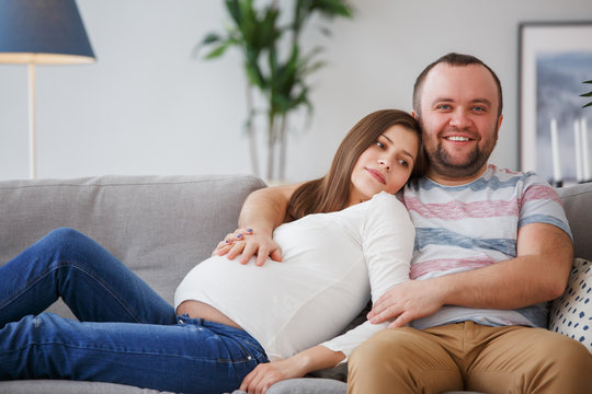 Photo of happy future parents sitting on gray sofa