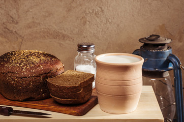Rye bread with salt on a cutting board, ceramic pot with milk and a kerosene lantern. Still-life in the rustic style