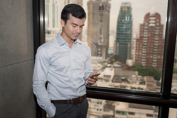 Handsome businessman using on the phone in office with cityscape background.