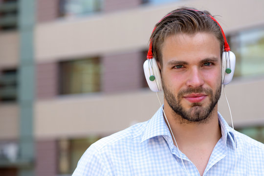 Young man listening music with headphones on urban background, defocused.