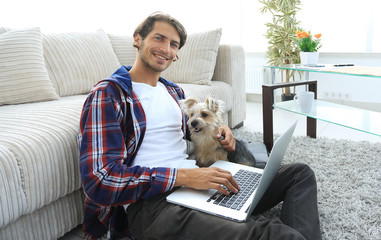 handsome guy with laptop hugging his dog and sitting near the couch