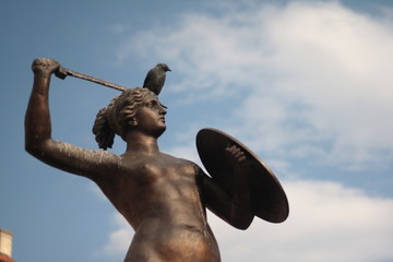 Mermaid statue Syrenka of Warsaw in Old Town Market Square, Poland. Statue has a bird on her head and blue sky in the background. © silvia