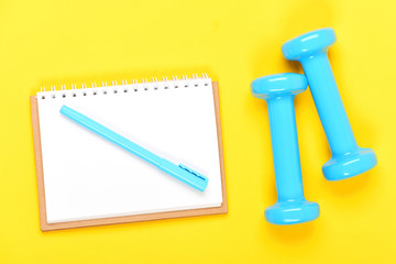 Notebook, pen and gym equipment top view on yellow background