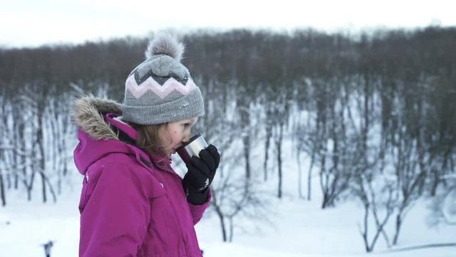 Little girl drinking hot drink outdoors in winter day