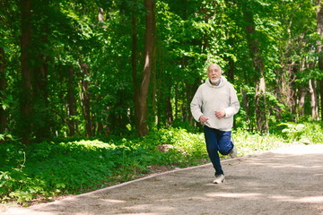 Elderly man running in green forest, copy space