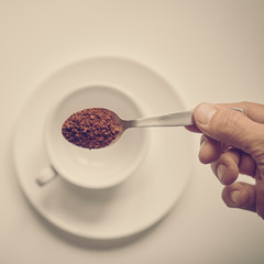 Making instant coffee. Closeup of hand putting spoon of instant coffee in cup, image with warm vintage toning
