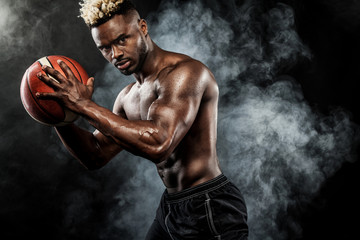 Portrait of afro-american sportsman, basketball player with a ball over black background. Fit young...