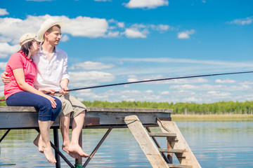 young happy couple on a pier fishing on a beautiful lake