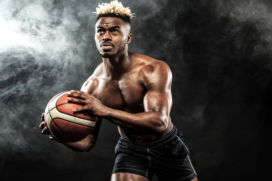 Portrait of afro-american sportsman, basketball player with a ball over black background. Fit young man in sportswear holding ball.