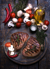 Grill Beef Steak, salt, pepper, garlic, rosemary, tomatoes, mushroom, olive oil  on the dark wooden board, background.