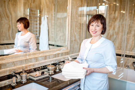 Portrait of a senior chambermaid standing with clean towels in the hotel bathroom