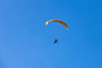 Yellow moto-paraglider flying over clear blue sky