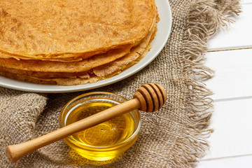 A pile of pancakes, honey, for the celebration of the carnival. Thin pancakes for breakfast. Pancakes and honey Maslenitsa. Pancakes with honey on a white wooden background. space for text