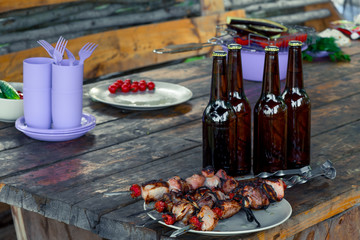 tasty shish kebab on a plate and a bottle of beer stand on a wooden table on a picnic
