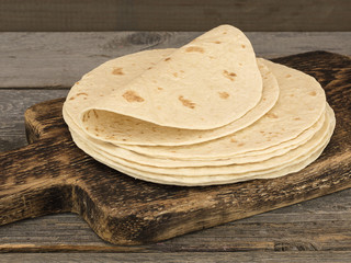 Board with stack of yummy tortillas on wooden table. 