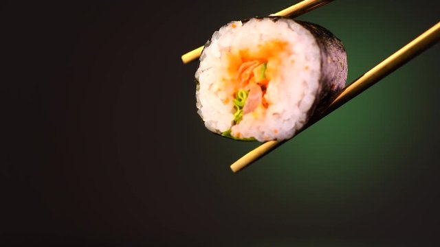 Sushi roll in chopsticks over black background. Seafood. Healthy eating, dieting concept. 4K UHD video footage. 3840X2160